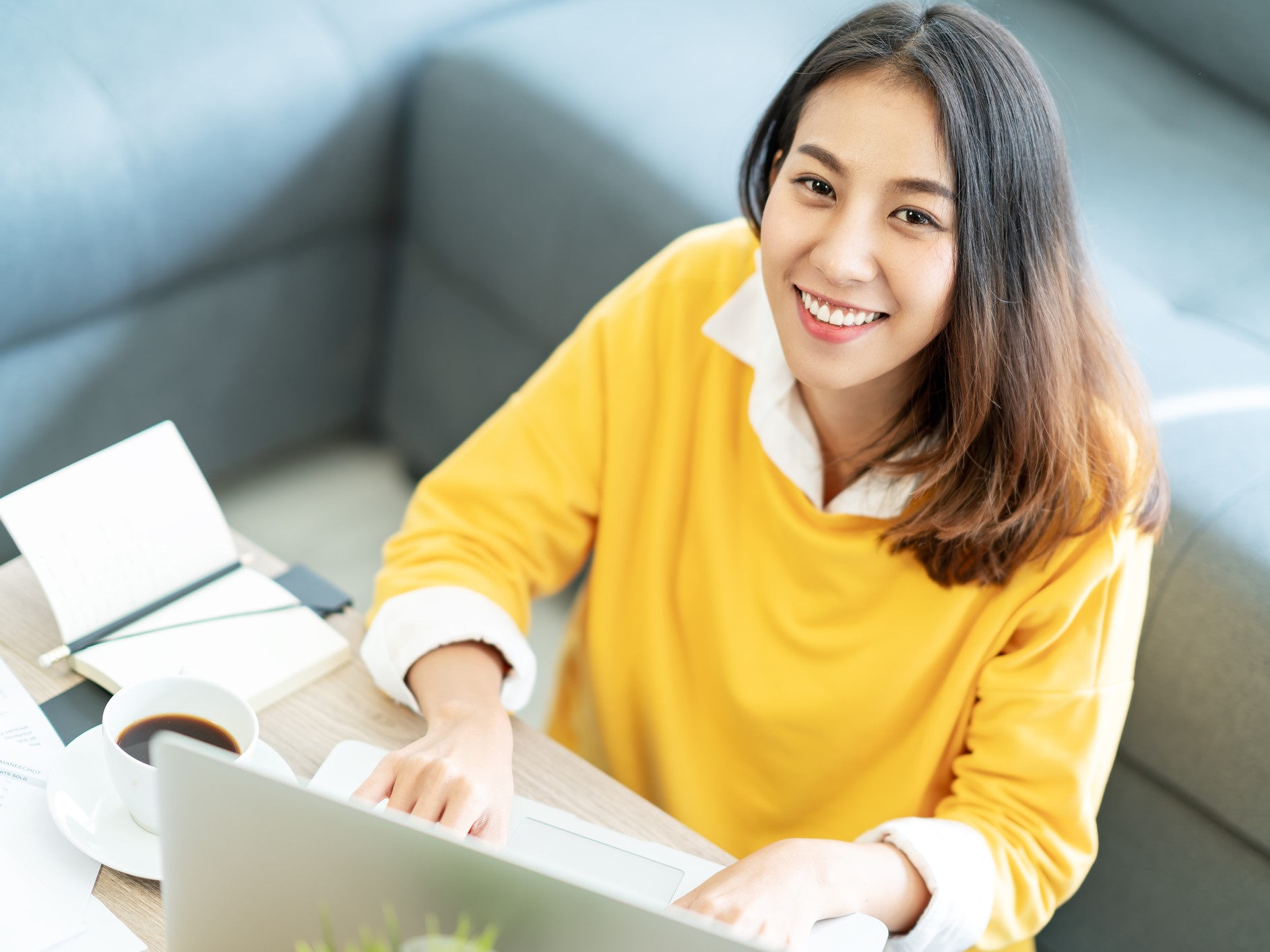 Young attractive happy asian female student sitting at living room floor smiling and looking up at camera working on laptop at home office. Young startup entrepreneur or freelance business concept.