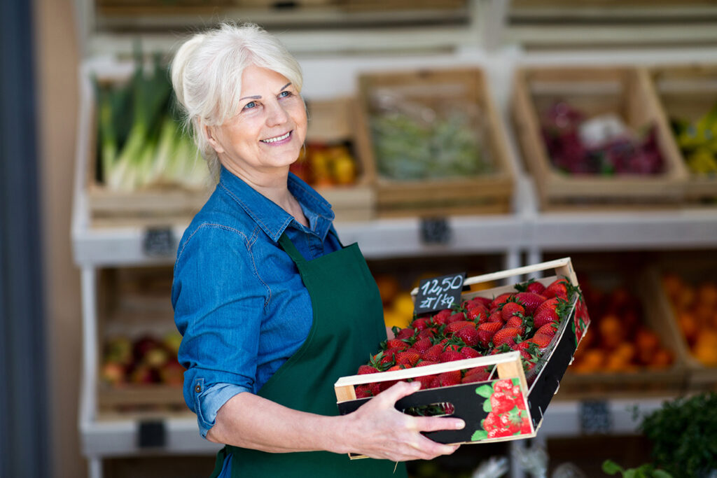 Shop assistant holding box with fresh strawberries in organic produce shop
