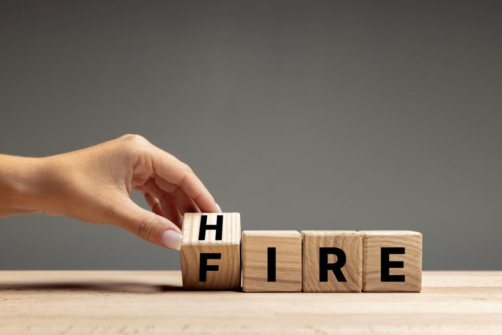 Difficult choice. Female hand flips wooden cubes with word fire to hire over grey background. Management and process for business success