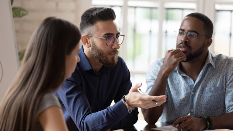 In board room gathered multi racial business people focus on serious middle eastern ethnicity team leader talking about strategy, corporate goals, share ideas, solve problems together at group meeting