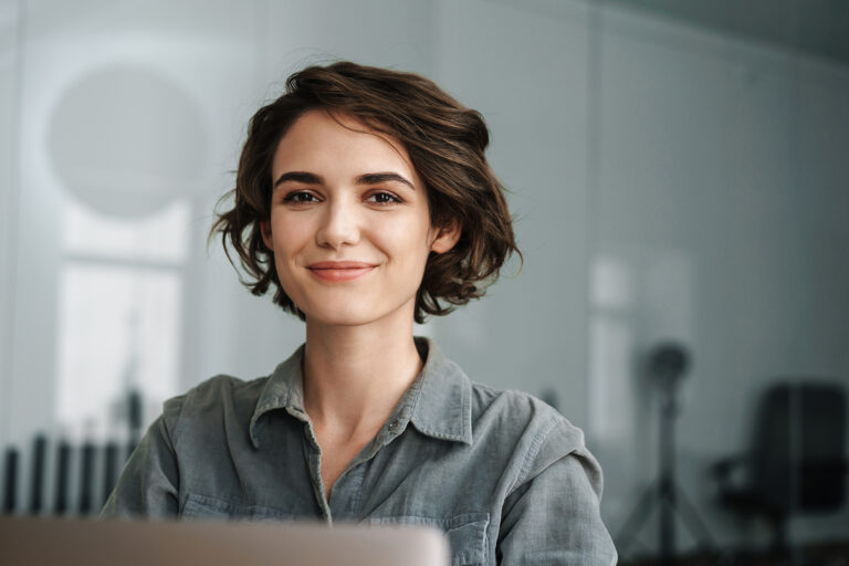 Image of young beautiful joyful woman smiling while working with laptop in office