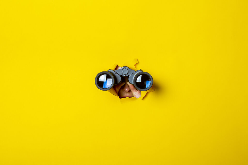Female hand holds black binoculars on a yellow background. Journey, find and search concept