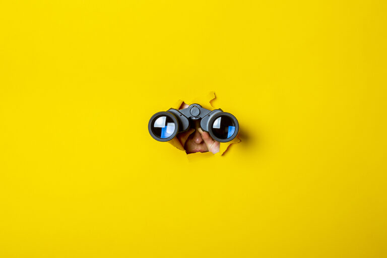 Female hand holds black binoculars on a yellow background. Journey, find and search concept