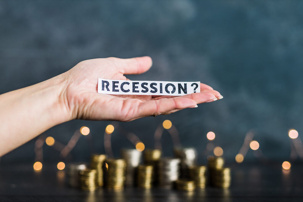 recession and inflation after the Covid-19 pandemic conceptual image, hand holding Recession text in front of stacks of coins with fairy lights in the background